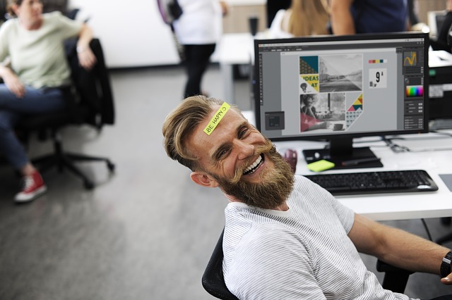 Imagem de homem sorrindo no escritório com um adesivo na testa dizendo: "Be happy". Experiência do consumidor está moldando o local de trabalho.