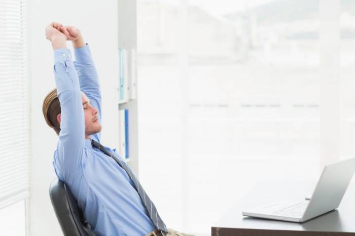 Imagem homem alongando-se em sua mesa de trabalho.