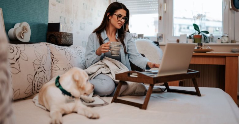 Foto moça sentada no sofá trabalhando com seu cachorro ao lado.
