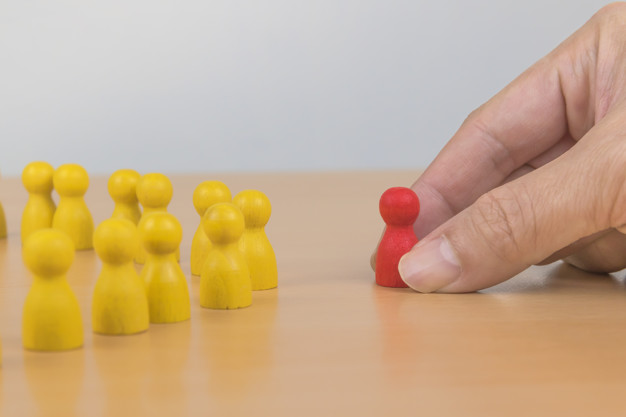 Imagem mão segurando boneco vermelho diante de outros amarelos. Personas de clientes.