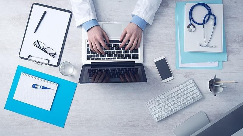 Foto médico à mesa em frente a notebook, atendimento ao cliente na área da saúde.