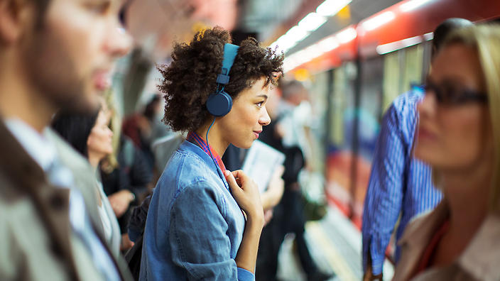 Moça esperando metrô e ouvindo podcasts sobre atendimento ao cliente e tecnologia